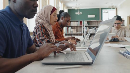 一群不同种族的学生坐在移民教育中心的桌子旁，上课时使用笔记本电脑