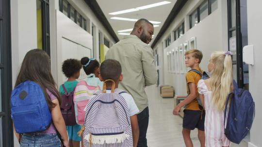 非裔美国男教师和不同学生在学校大厅散步的背影视频视频素材模板下载