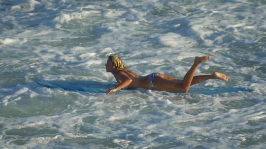 一名年轻女子穿着比基尼在长板冲浪板上冲浪。