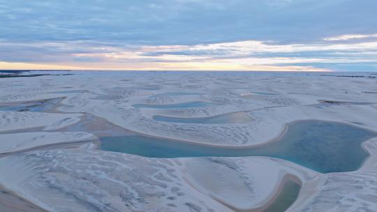 无人机飞越巴西东北部被白色沙丘包围的蓝色泻湖