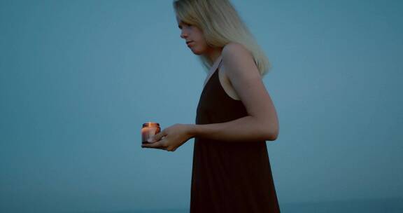 在傍晚天空下拿着蜡烛的黑裙女人走路