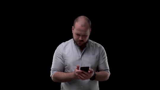 穿着衬衫的秃头胡子男人看着手机。他非常惊讶，用绿屏显示手机视频素材模板下载