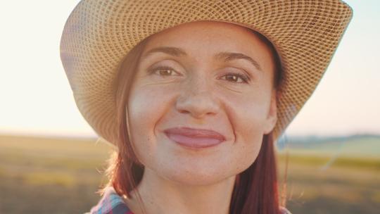 日落时分，戴着帽子的女农民在工作日后看着相机的特写肖像。农业商业概念