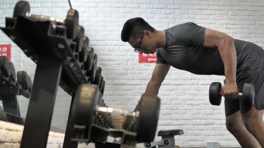 男子在健身房使用哑铃锻炼背部肌肉