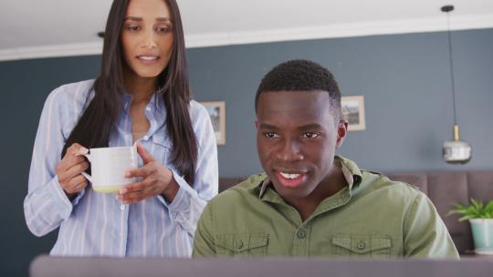 幸福多样化的夫妇在卧室喝咖啡，一起看笔记本电脑屏幕的视频