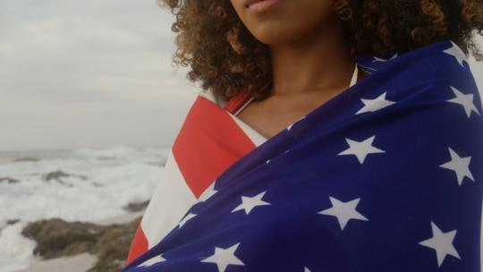站在海滩上裹着美国国旗的非裔美国妇女的正视图4k