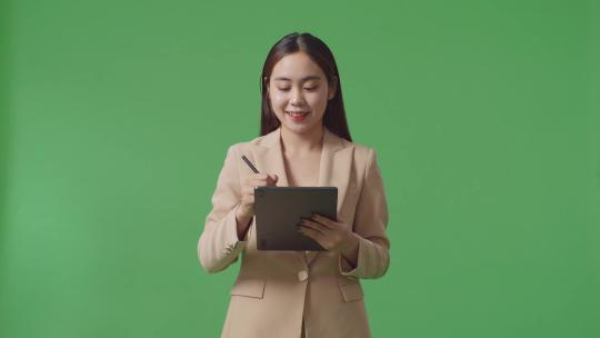 一名亚洲女商人在工作室的绿屏背景上写平板电脑