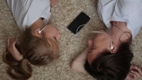 有趣的镜头显示，年轻女子和小女儿躺在地板上，互相看着对方，用一个耳机听电话里的音乐。