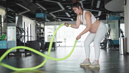 怀孕的妇女在健身房练习战绳锻炼身体