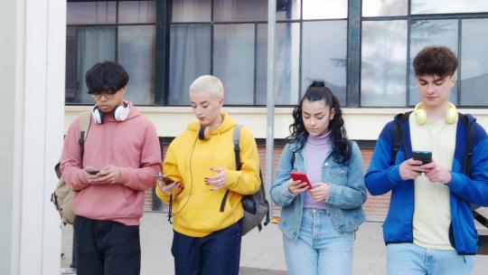 一群青少年学生一边看智能手机一边走路