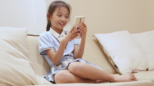 坐在沙发上玩手机开心大笑的小女孩视频素材模板下载