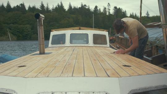 年轻的木匠擦拭木制船宿船的砂纸甲板