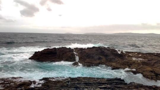 大海在一个多风多云的日子里，海浪在岩石上快速起泡，乌云密布。Poin