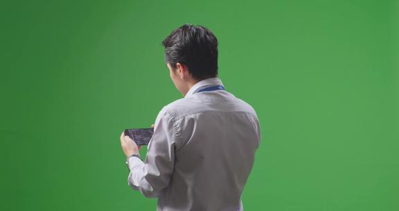 亚洲商人在工作室的绿屏背景下使用手机的后视图