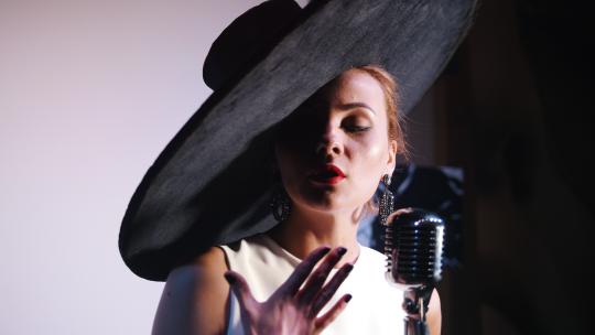 一个戴着黑色优雅大帽子的女人站在麦克风后面唱歌