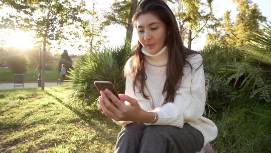 年轻的女性在草地上玩手机