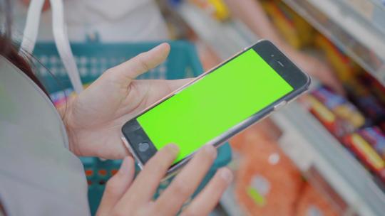 女人在超市使用绿屏手机查询商品价格