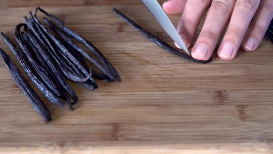 用刀在木制砧板上切香草豆