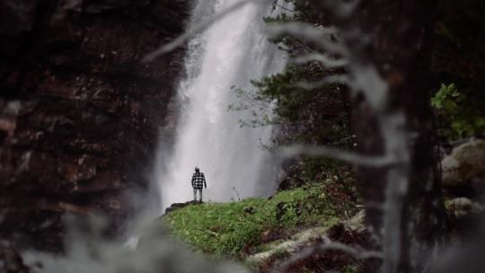 男人站在一个巨大的瀑布前，白天慢动作拍摄一个美丽的位置。