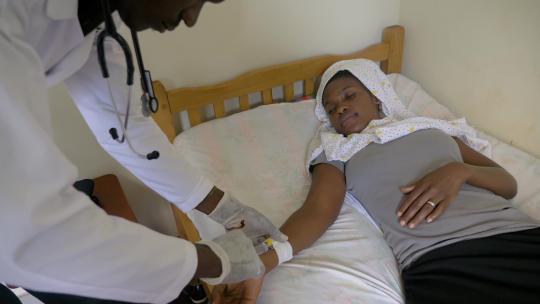 一张照片俯视着一名穿着白色实验室外套的非洲男医生给一名非洲妇女注射