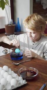 一个男孩从一碗蓝色液体中舀出彩色的鸡蛋  竖屏