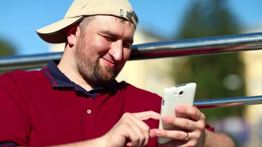 戴棒球帽的男人使用智能手机特写。手里拿着白色手机的胖子