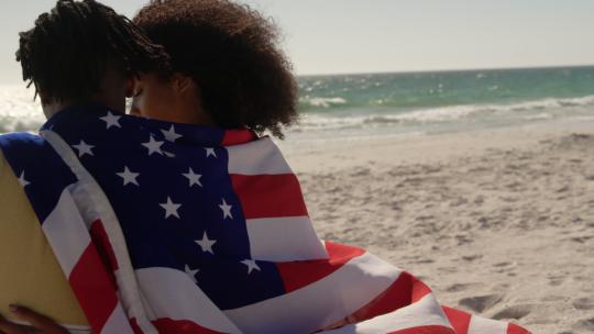 裹着美国国旗的夫妇坐在海滩