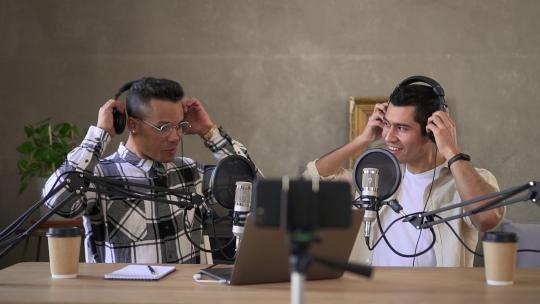 商人录制商业播客，在笔记本电脑前挥手，坐在桌子旁spbd。年轻的拉丁男人戴上耳机直播，在电脑屏幕前挥手，坐在办公桌前