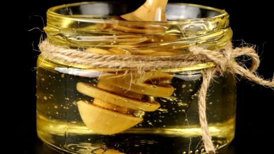 蜂蜜从勺子纺锤上流下来，进入一个黑色背景上有蜂蜜的罐子。视频素材模板下载