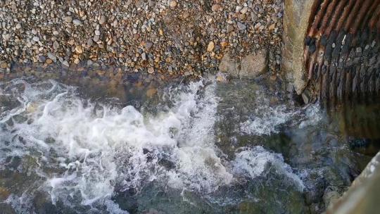 水从石墙的排水管倾泻而下，穿过西威尔士布罗德海文的石质海滩