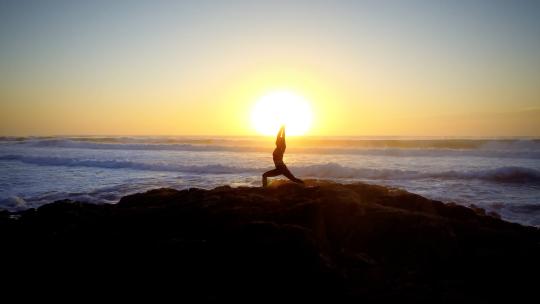 航拍清晨海边岩石上做瑜伽的女人海浪日出
