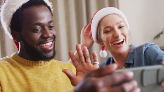 快乐的一群不同的朋友在圣诞派对上使用智能手机进行视频通话