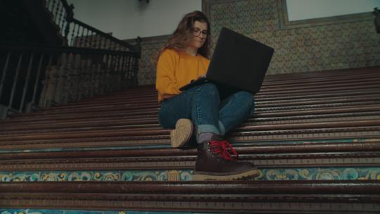 女性坐在台阶上用笔记本电脑打字