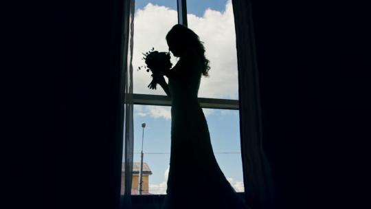 在窗前拿着花束的新娘剪影