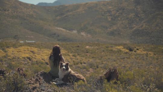 女孩与狗相伴依靠在大山里看风景