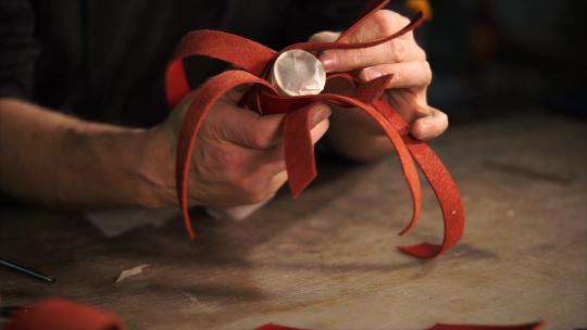 工作室专业皮革工人的工作过程。他小心翼翼地用红色编织皮革条纹覆盖管子。