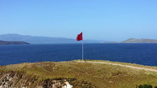 无人机拍摄的土耳其国旗在海边随风飘扬。这片土地被小灌木丛覆盖。