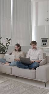 一对夫妇坐在沙发上使用笔记本电脑竖屏