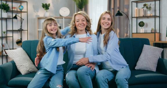 母亲和她的两个女儿在沙发在拥抱