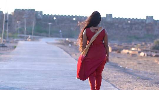 身穿红裙的女孩在路上行走的背影