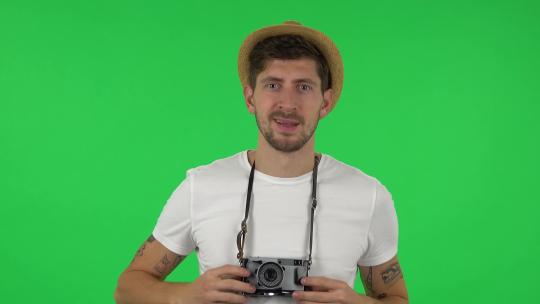 度假戴帽子的游客肖像在复古相机上拍照。绿屏