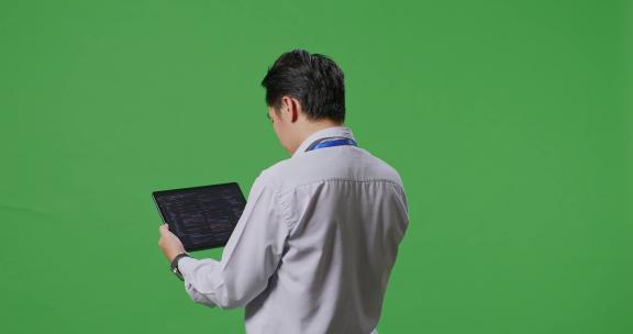 亚洲商人在工作室的绿屏背景上使用平板电脑的后视图
