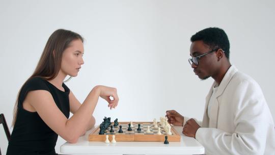 一个白人年轻女孩和戴眼镜的非裔美国人下棋和大笑