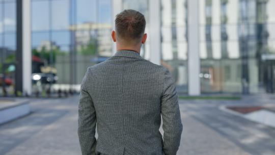 成功的高加索男性高级经理通勤上班，后视。一位英俊的30岁高级经理穿着古典西装走向办公中心的后视。商务人士概念
