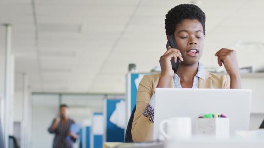 非裔美国女商人在办公室使用笔记本电脑和智能手机，慢动作