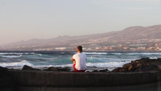 一个人坐在墙上看着海浪上岸
