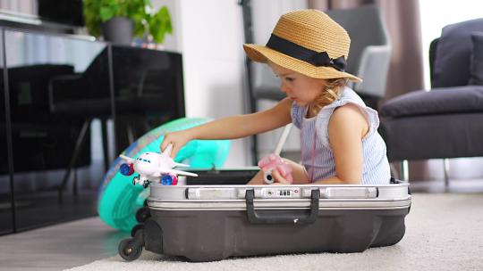 坐在行李箱里玩玩具飞机的小女孩
