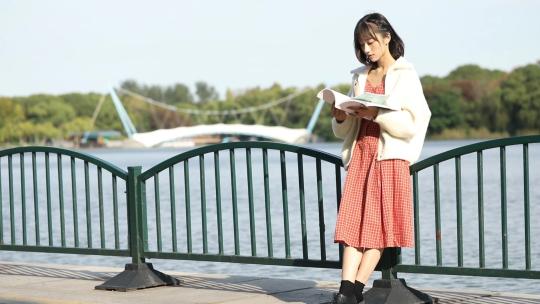 站在河边栏杆上看书的女生