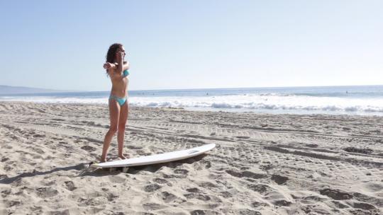 一个女冲浪者在海滩上伸展身体
