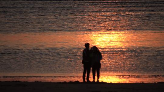 海边沙滩上看金色海面的一对情侣视频素材模板下载